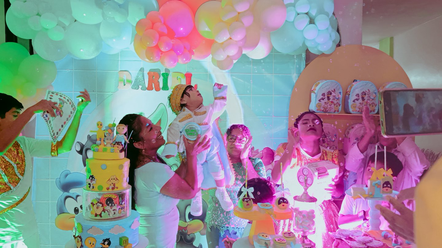 A woman holds a child near cartoon themed birthday decorations.
