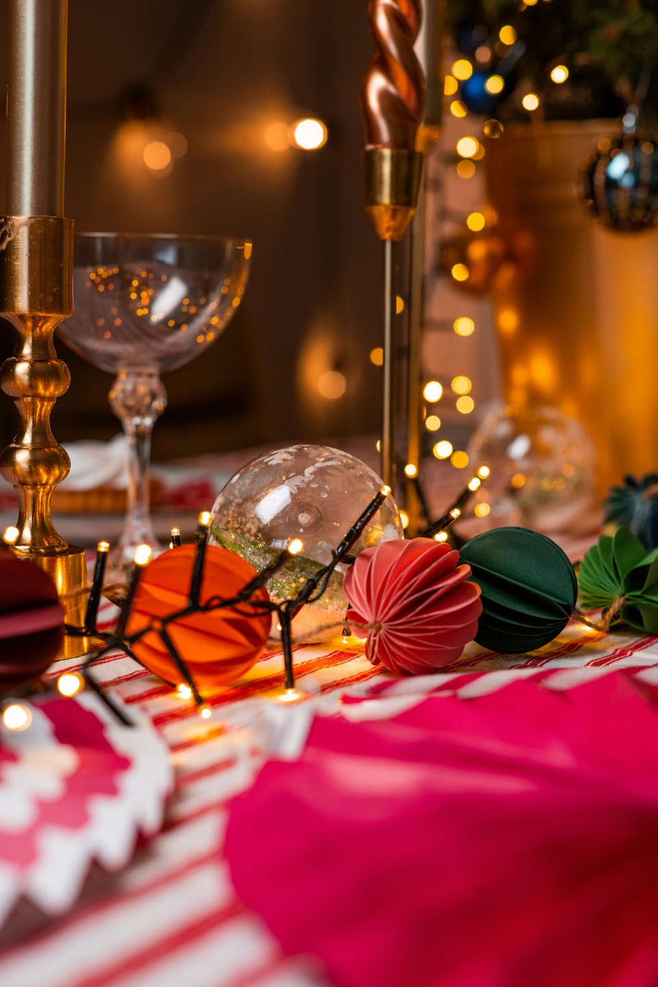 Holiday table setting with candles and ornaments on a striped tablecloth.
