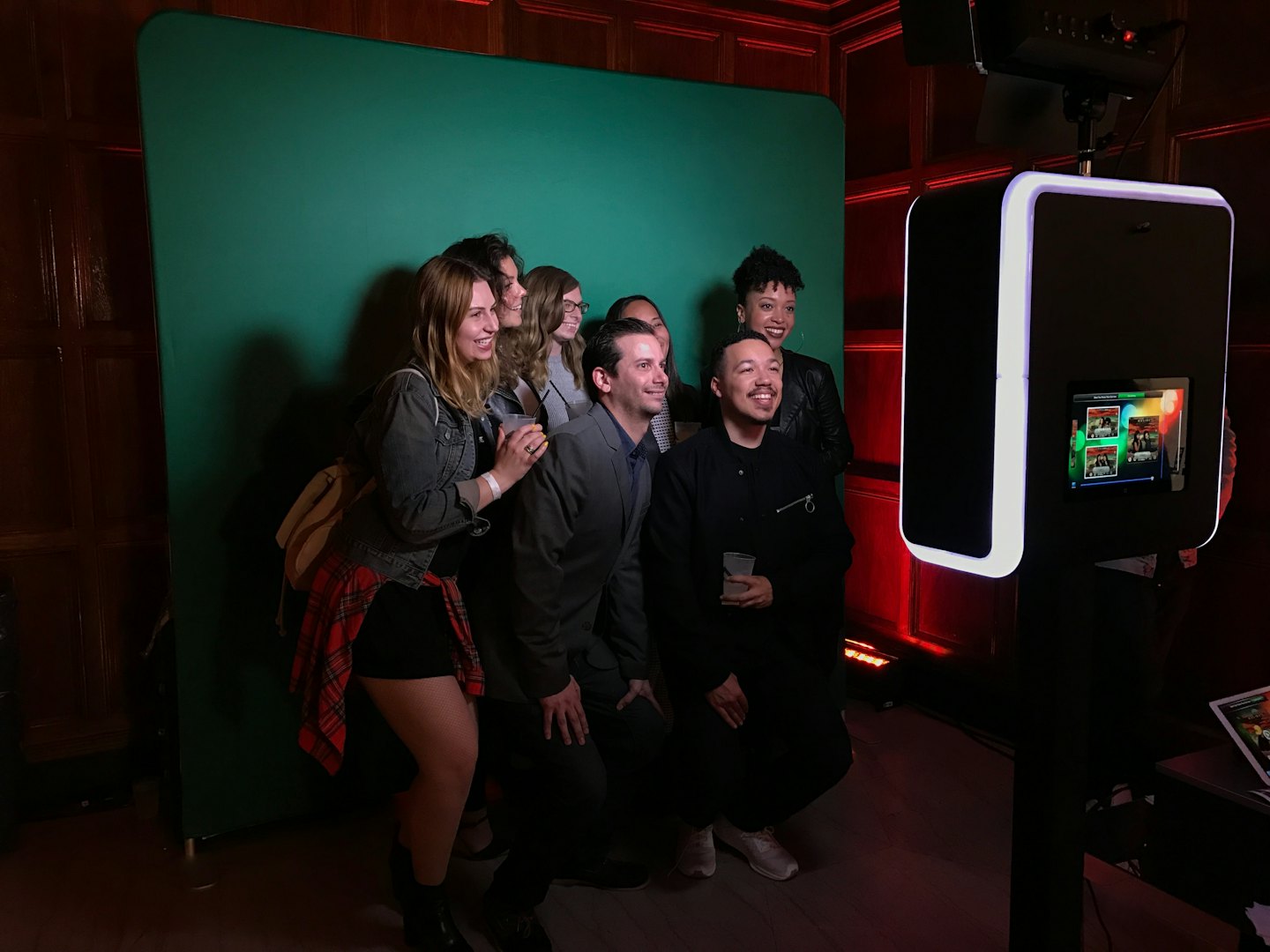 A group of friends smiles in front of a black photo booth.